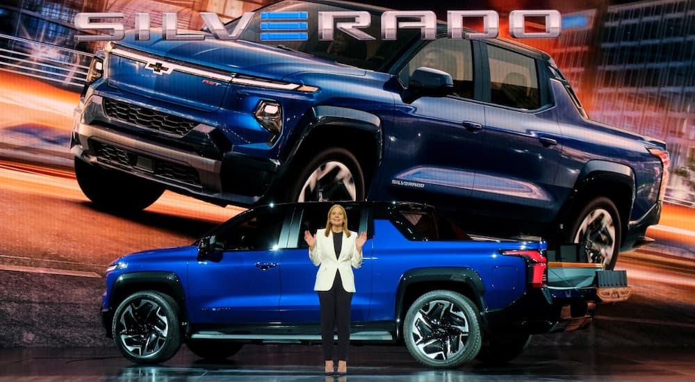 A blue 2024 Chevy Silverado EV is shown from the side on a stage.