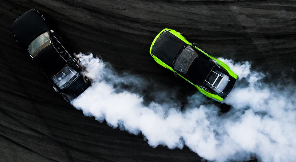 A black and a green car are shown drifting from a high angle.