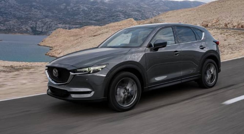 A grey 2022 Mazda CX-5 is shown from the front at an angle as it drives down a road in the desert.
