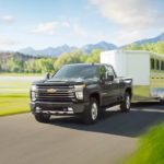 A black 2022 Chevy Silverado 3500HD is shown towing a horse trailer on an open road.