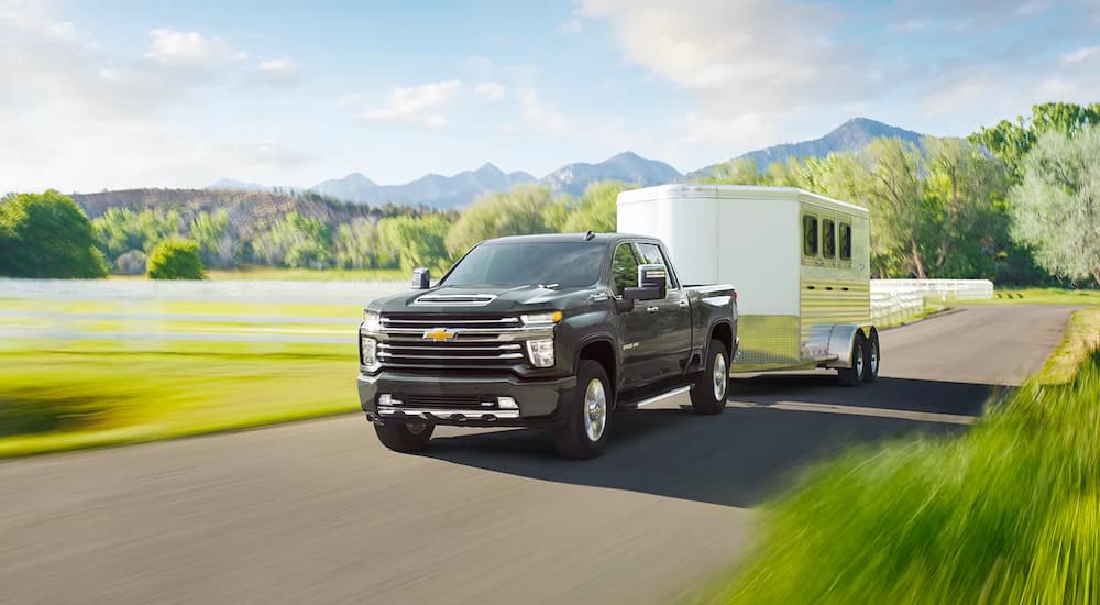 A black 2022 Chevy Silverado 3500HD is shown towing a horse trailer on an open road.