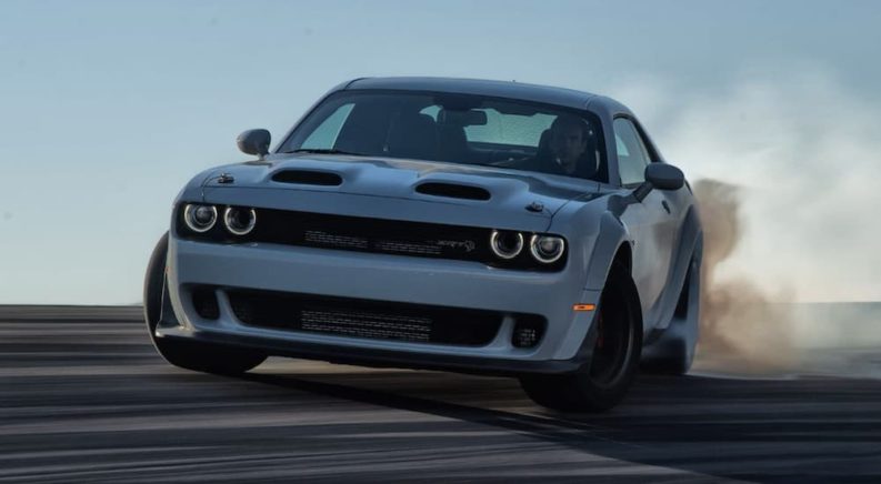 A white 2022 Dodge Challenger Hellcat is shown from the front doing a burn out.