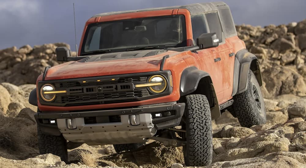An orange 2022 Ford Bronco Raptor is shown off-roading on rocky terrain.
