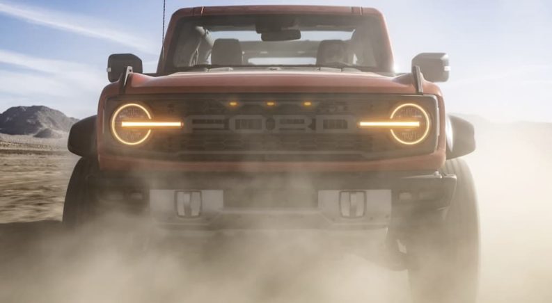 A 2022 Ford Bronco Raptor is shown from the front during a dust storm in the desert.