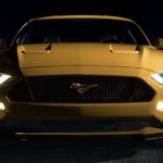 A yellow 2022 Ford Mustang GT is shown from the front in a dark warehouse.