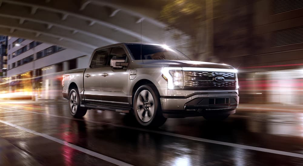 A silver 2022 Ford F-150 Lightning is shown from the front driving through a city at night.