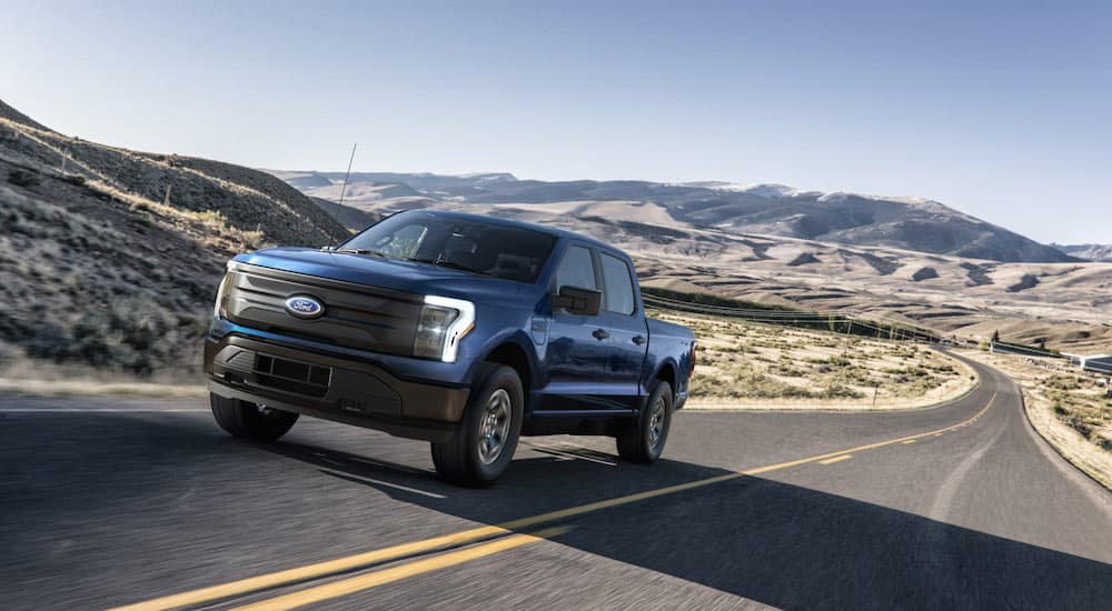 A blue 2022 Ford F-150 Lightning is shown from the front on a desert highway.