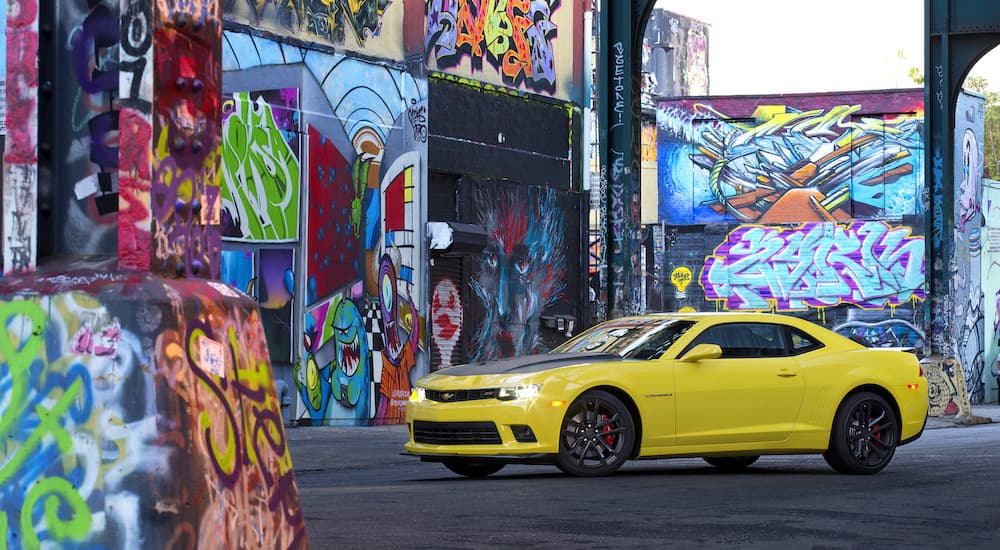 A yellow 2014 Chevy Camaro 1LE is shown parked next to walls with graffiti.
