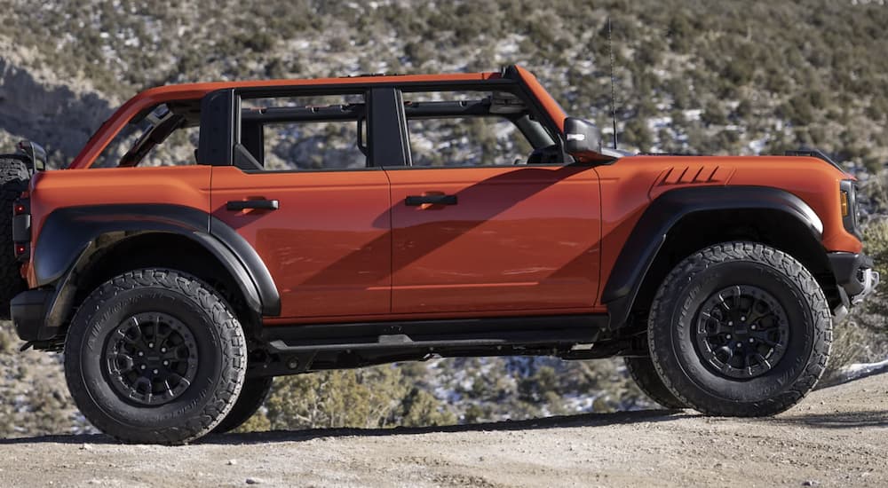 An orange 2022 Ford Bronco is shown from the side driving in the mountains after leaving a Ford Bronco dealer near you.