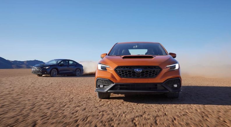 A grey 2022 Subaru WRX GT and an orange Limited are shown on dirt.