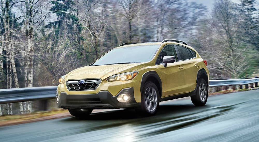 A yellow 2022 Subaru Crosstrek Sport is shown from the front driving on an open tree lined road after leaving a Subaru dealer.