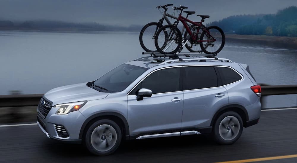 A white 2022 Subaru Forester is shown driving past a body of water after elaving a Subaru dealer.
