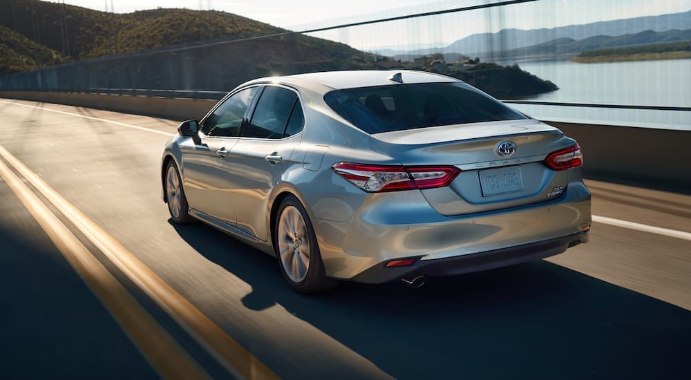 A grey 2020 Toyota Camry Hybrid XLE is shown from the rear driving on an open road.