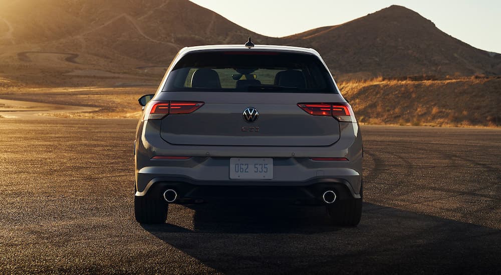 A light grey 2022 Volkswagen Golf GTI is shown from the rear parked in front of a mountain.