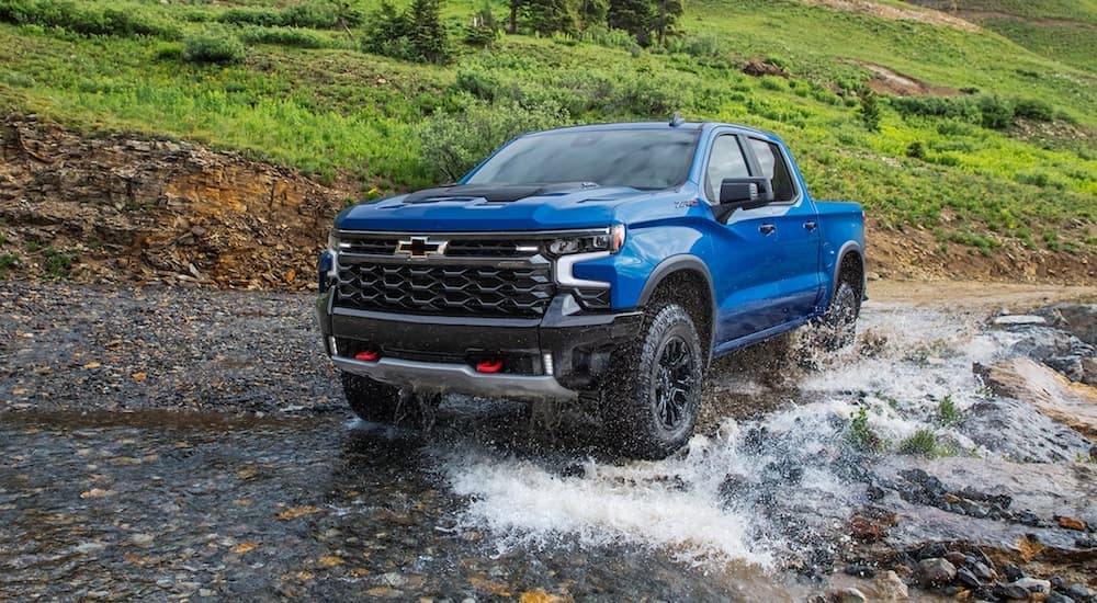 A blue 2022 Chevy Silverado 1500 ZR2 is shown from the front off-roading through a river after leaving an off-road truck dealer.