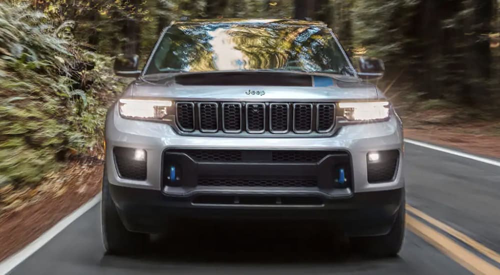 A silver Jeep Grand Cherokee 4xe is shown from the front driving on a tree lined road.