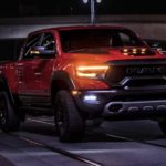 An orange 2022 Ram 1500 TRX is shown from the front driving through a city at night after visiting a Ram dealer.