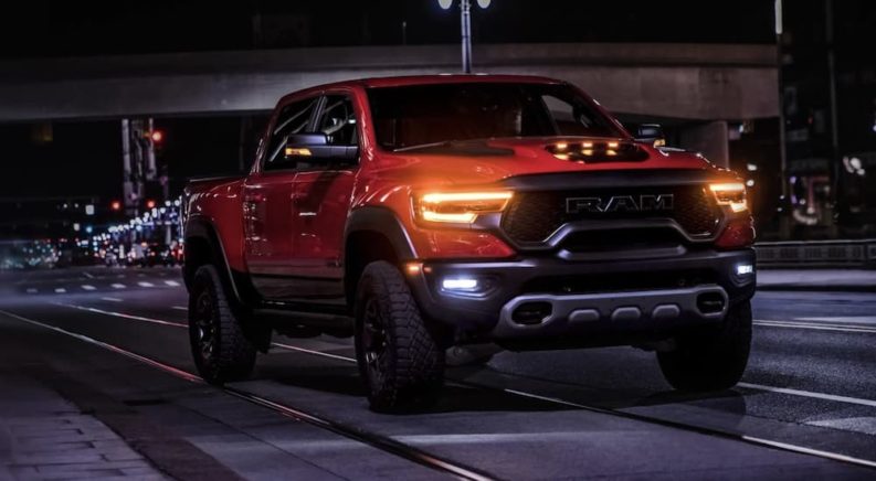 An orange 2022 Ram 1500 TRX is shown from the front driving through a city at night after visiting a Ram dealer.