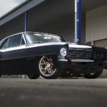 A black 1967 Chevy Nova is shown from the side parked in front of a building.