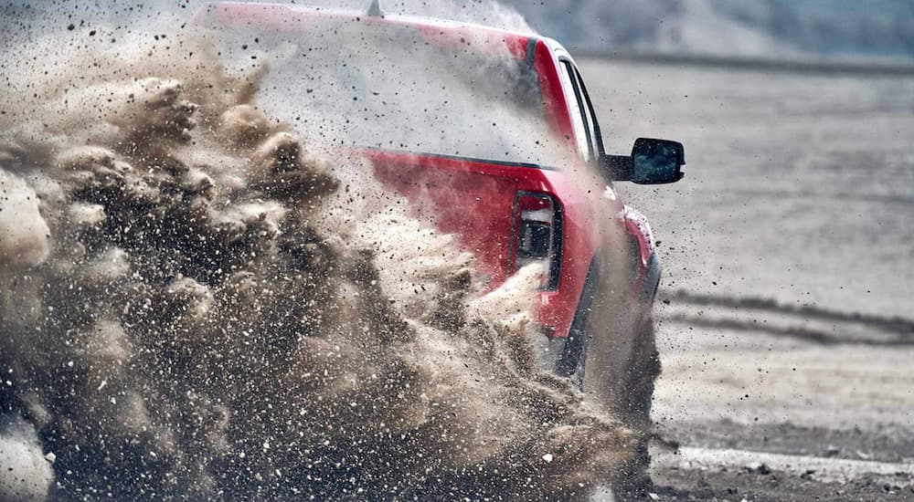 A red 2022 Ram 1500 TRX is shown from the rear as it drives through sand after the owner searched 'Ram dealer near me.'