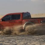 A red 2021 Ford F-150 Raptor is shown from the side while it slides through sand.