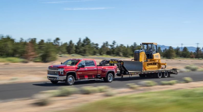 A red 2022 Chevy Silverado 3500 HD is shown from the side while it tows a trailer loaded with a bulldozer.