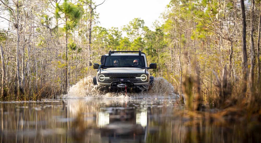 A green 2022 Ford Bronco Everglades is shown from the front while driving through mud after leaving a Shively Online Car Dealership.