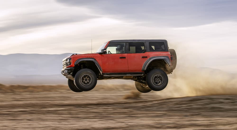 A red 2022 Ford Bronco Raptor is shown from the side while it flies off a jump off-road.