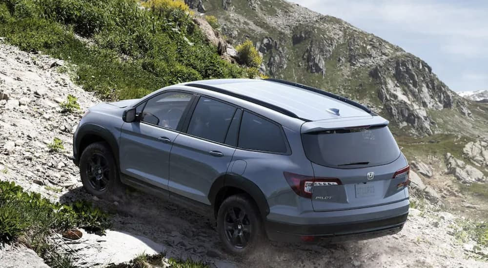 A grey 2022 Honda Pilot TrailSport is shown from the rear off-roading on a mountain.