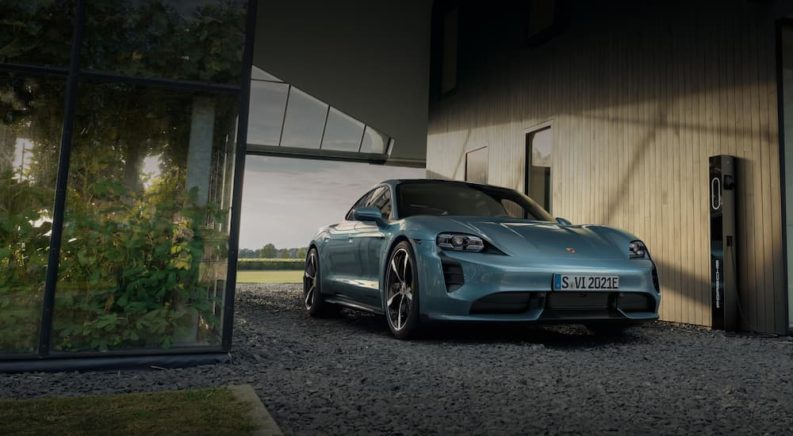 A light blue 2022 Porsche Tycan is shown at a house next to a Porsche charging station.