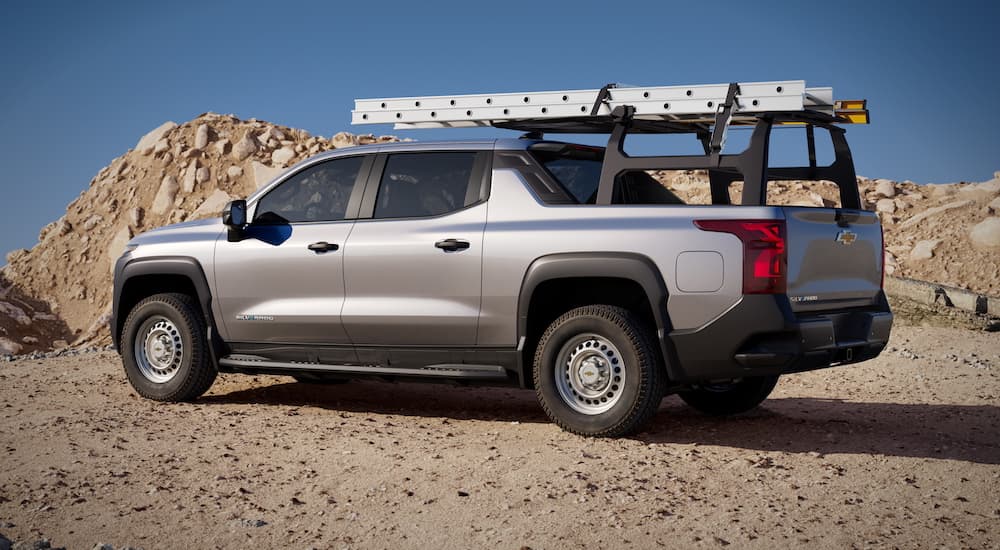 A 2024 Chevy Silverado EV WT equipped with a ladder rack is shown from the rear while it is parked in the dirt.