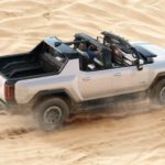 A white 2022 GMC Hummer EV is shown from the rear at a high angle while it drives through sand dunes.