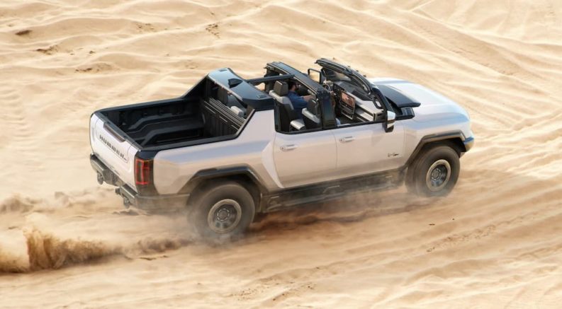 A white 2022 GMC Hummer EV is shown from the rear at a high angle while it drives through sand dunes.