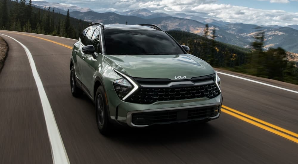 A green 2023 Kia Sportage is shown driving on an open mountain road.