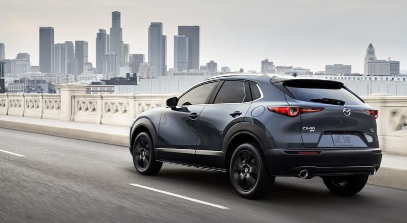 A grey 2022 Mazda CX-30 is shown from the rear driving on a city bridge after visiting a Mazda dealer.