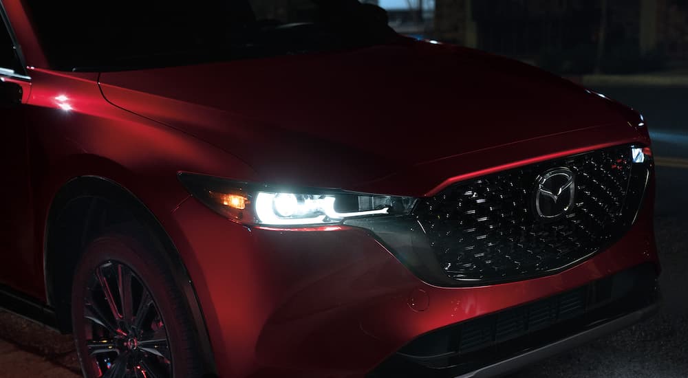 A close up shows the headlights and grille on a red 2022 Mazda CX-5 at night.