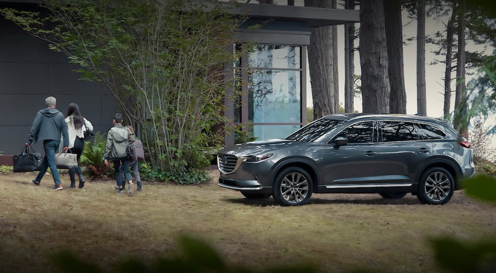 A grey 2022 Mazda CX-9 is shown from the side next to a family with luggage.