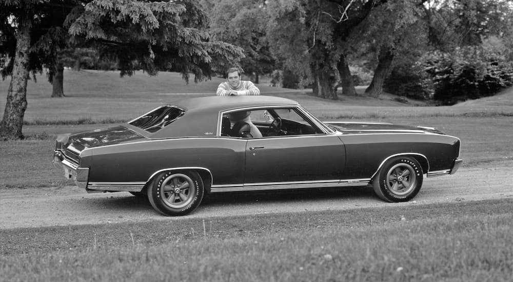 A black and white photo shows a 1971 Chevy Monte Carlo SS parked on a golf course.