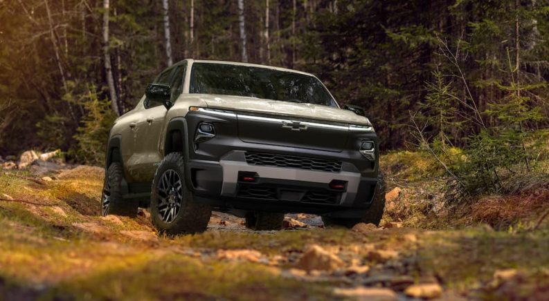 A tan 2024 Chevy Silverado EV TrailBoss is shown from the front while it drives offroad after leaving a Houston electric Silverado dealer.