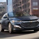 A black 2020 Chevy Malibu is shown from the front driving through a city.