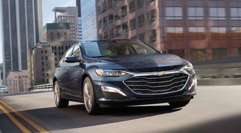 A black 2020 Chevy Malibu is shown from the front driving through a city.