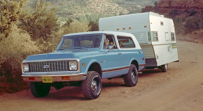 A blue 1969 Chevy Blazer is shown towing a trailer in the desert after leaving a used car dealer.