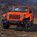 An orange 2019 Jeep Wrangler is shown from the front parked in the mountains.