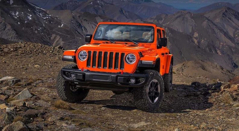 An orange 2019 Jeep Wrangler is shown from the front parked in the mountains.
