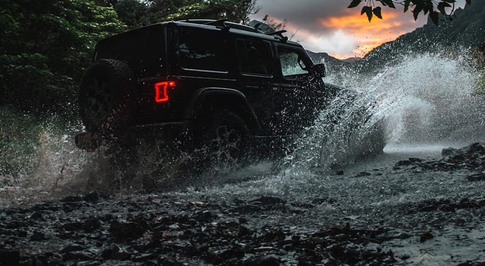 A black 2020 Jeep Wrangler unlimited is shown driving through a river after leaving a used car dealer near you.
