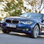 A blue 2015 BMW 340i is shown from the front at an angle while it drives down the road.