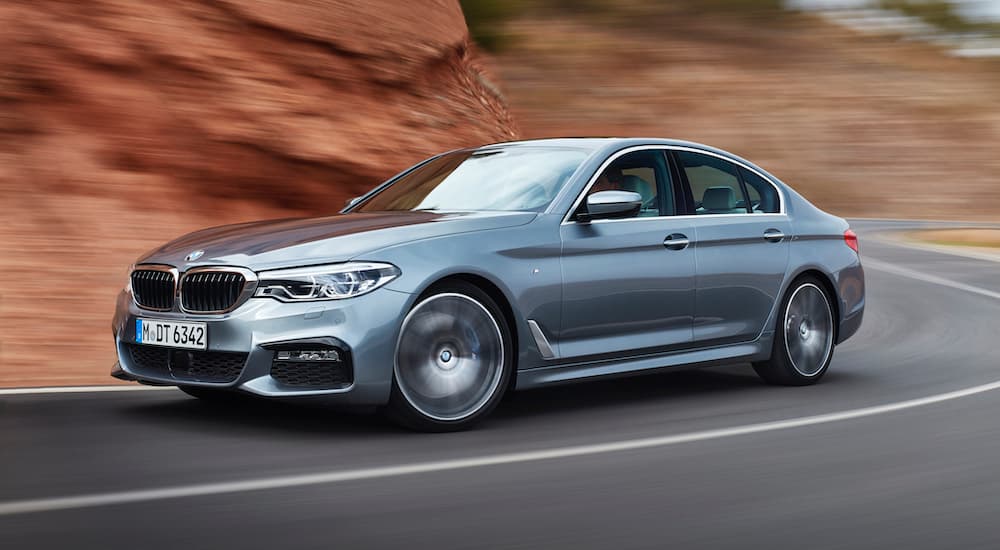A silver 2017 BMW 540i is shown from the side while driving down the road.