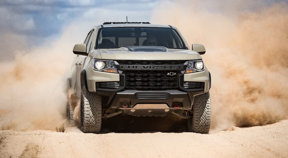 A tan 2022 Chevy Colorado ZR2 is shown from the front while driving through sand.
