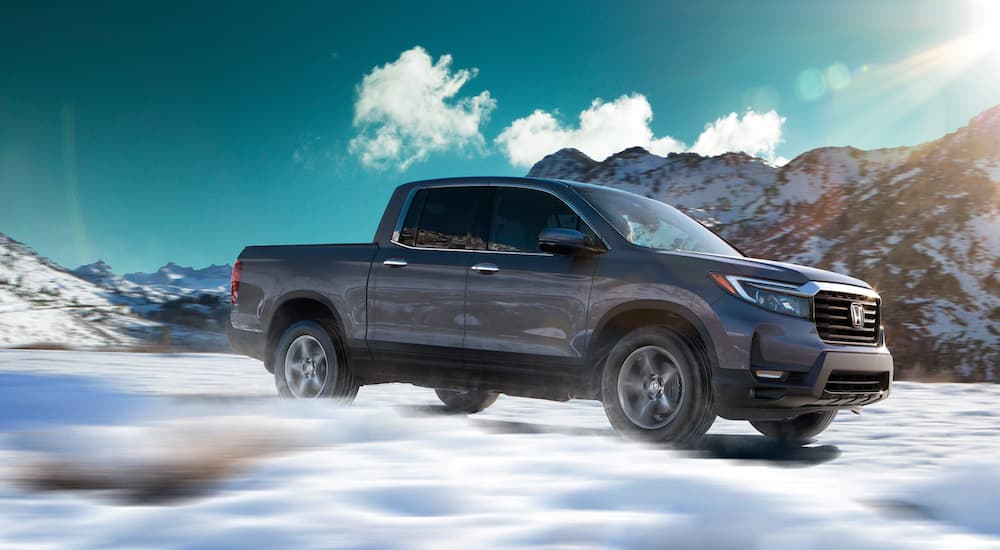 A grey 2022 Honda Ridgeline is shown from the side while driving through snow