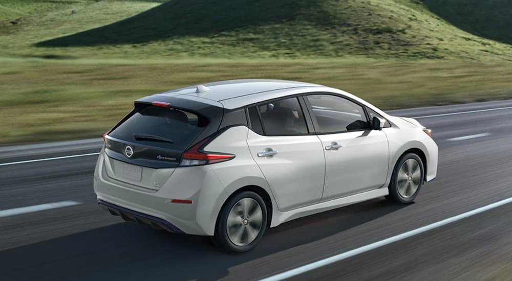 A white 2022 Nissan LEAF is shown from the rear at an angle while driving down the road.